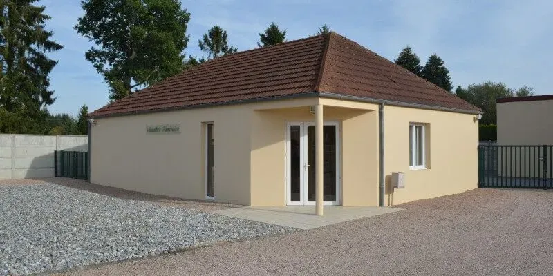 Façade d'une chambre funéraire moderne avec parking en gravier.